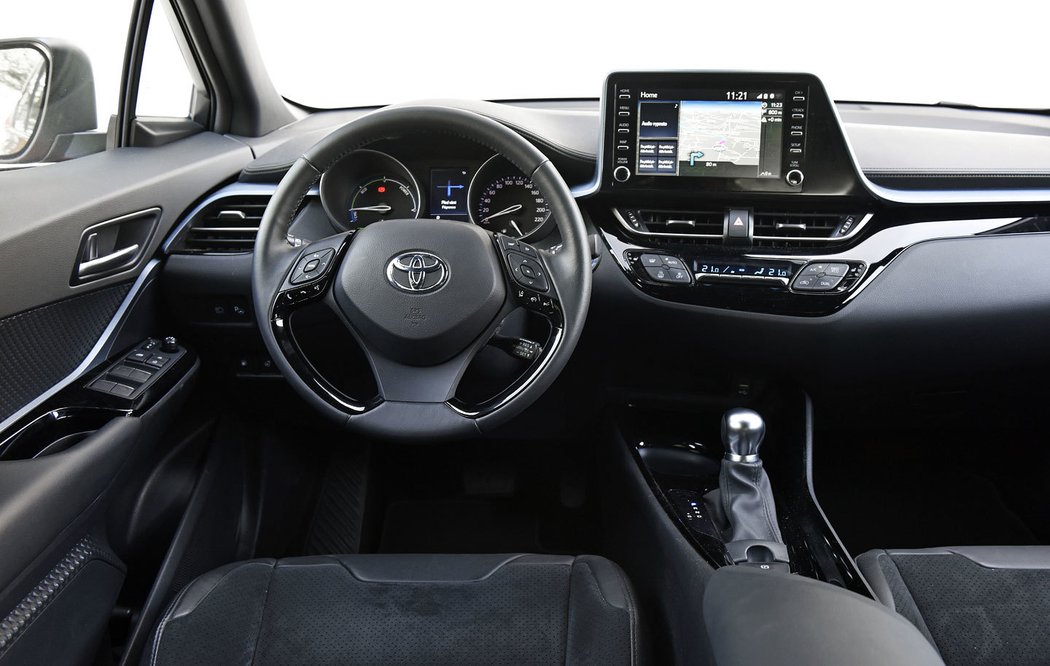 C-HR je v interiéru designově rozevláté stejně jako zvenku. Dekor dveří plynule přechází do palubní desky, v níž se proběhne i po hraně vystupující obrazovky. Toyota působí hravějším a stylovějším dojmem, ovšem také stísněnějším. Palubka je hluboká a zasahuje do prostoru spolujezdce.